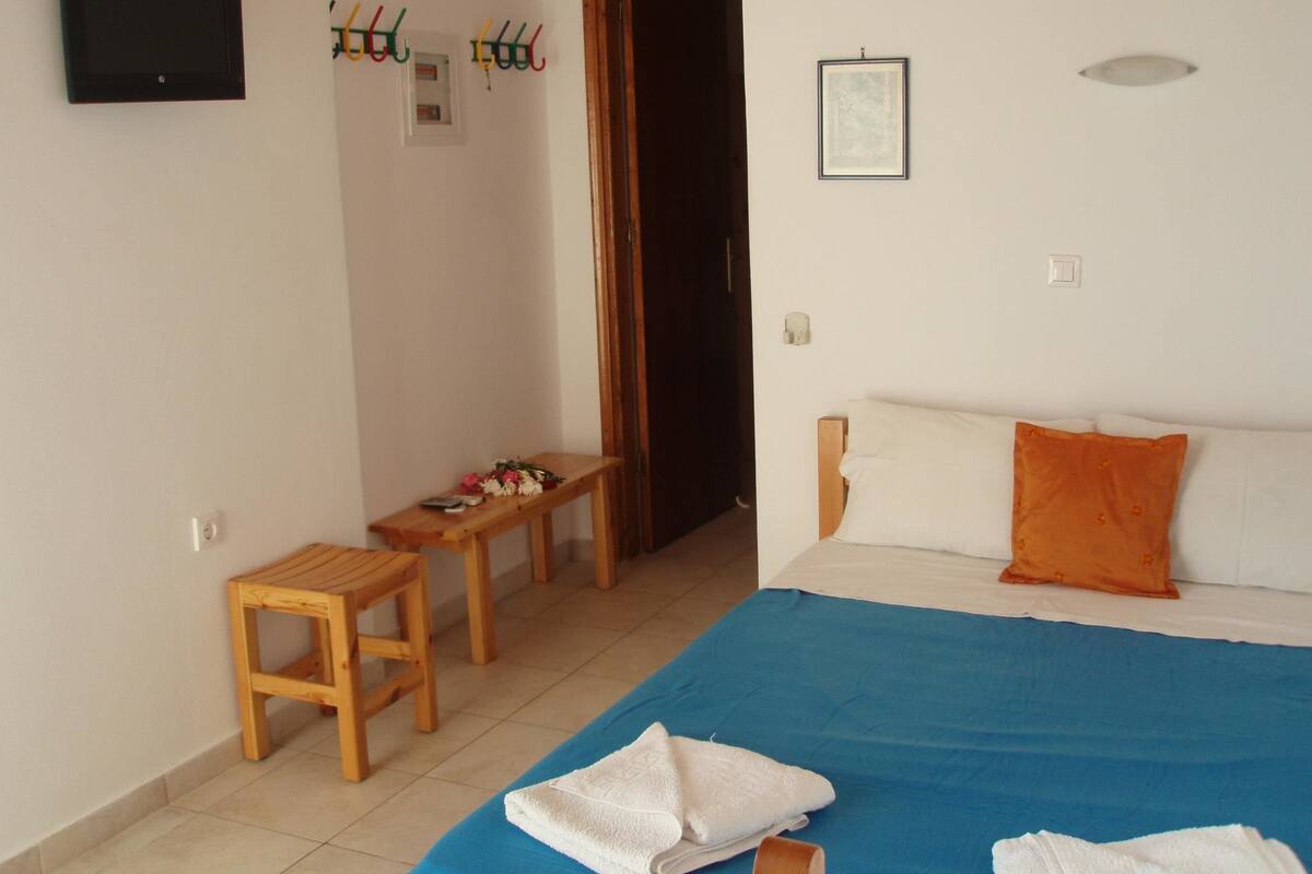 A bedroom with a bed, a wooden bench, a small table, a TV, and a door.