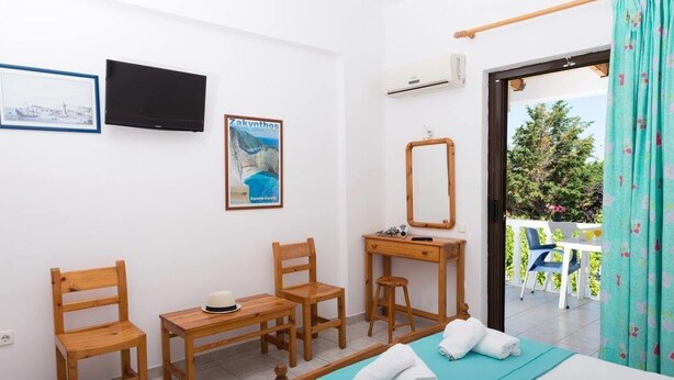 A bedroom with a bed, two wooden chairs, a small table, a mirror, and a poster on the wall. - Studio Stars (Zakynthos)