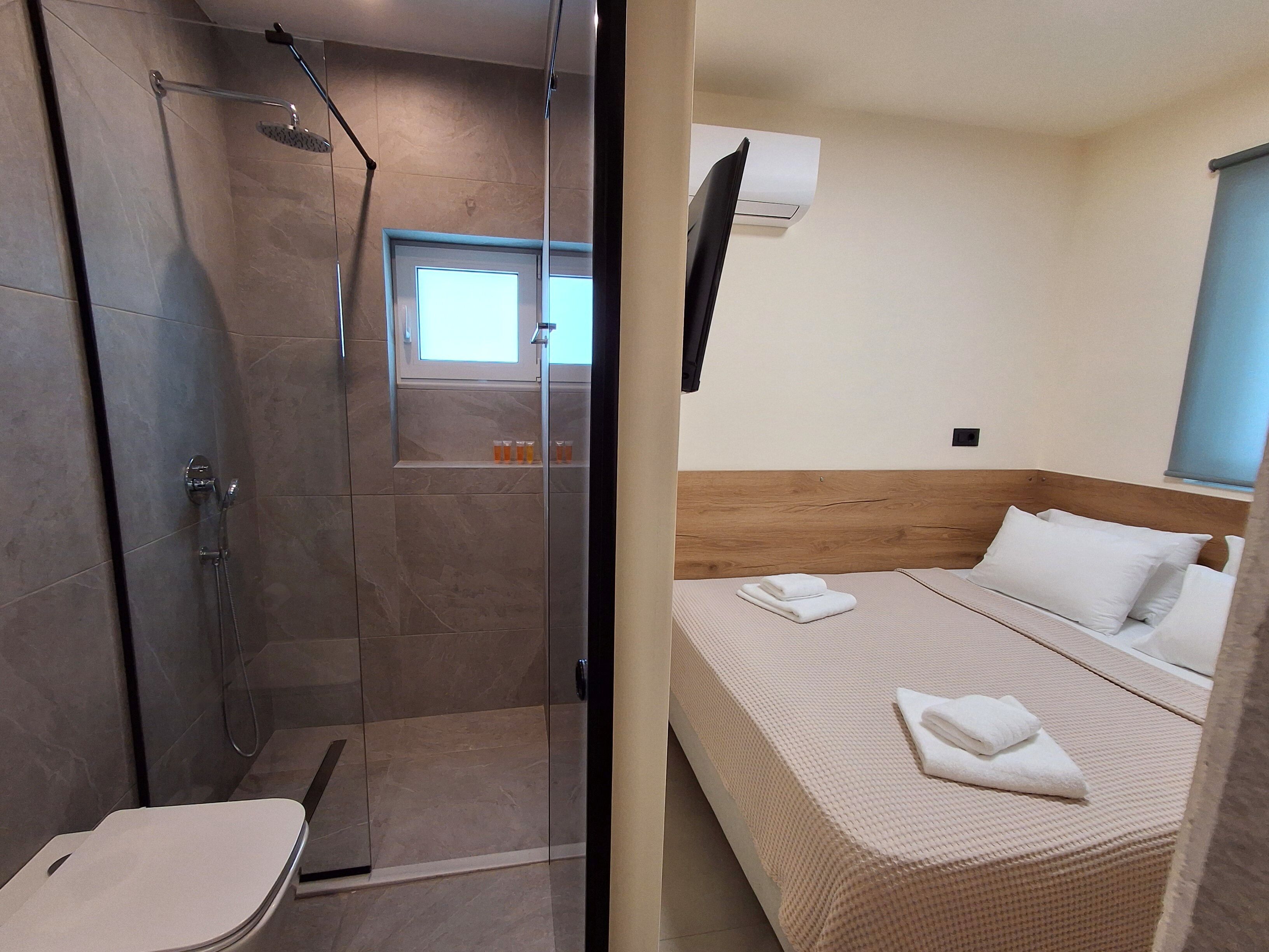 A bathroom with a shower, toilet, and a bed with a window.