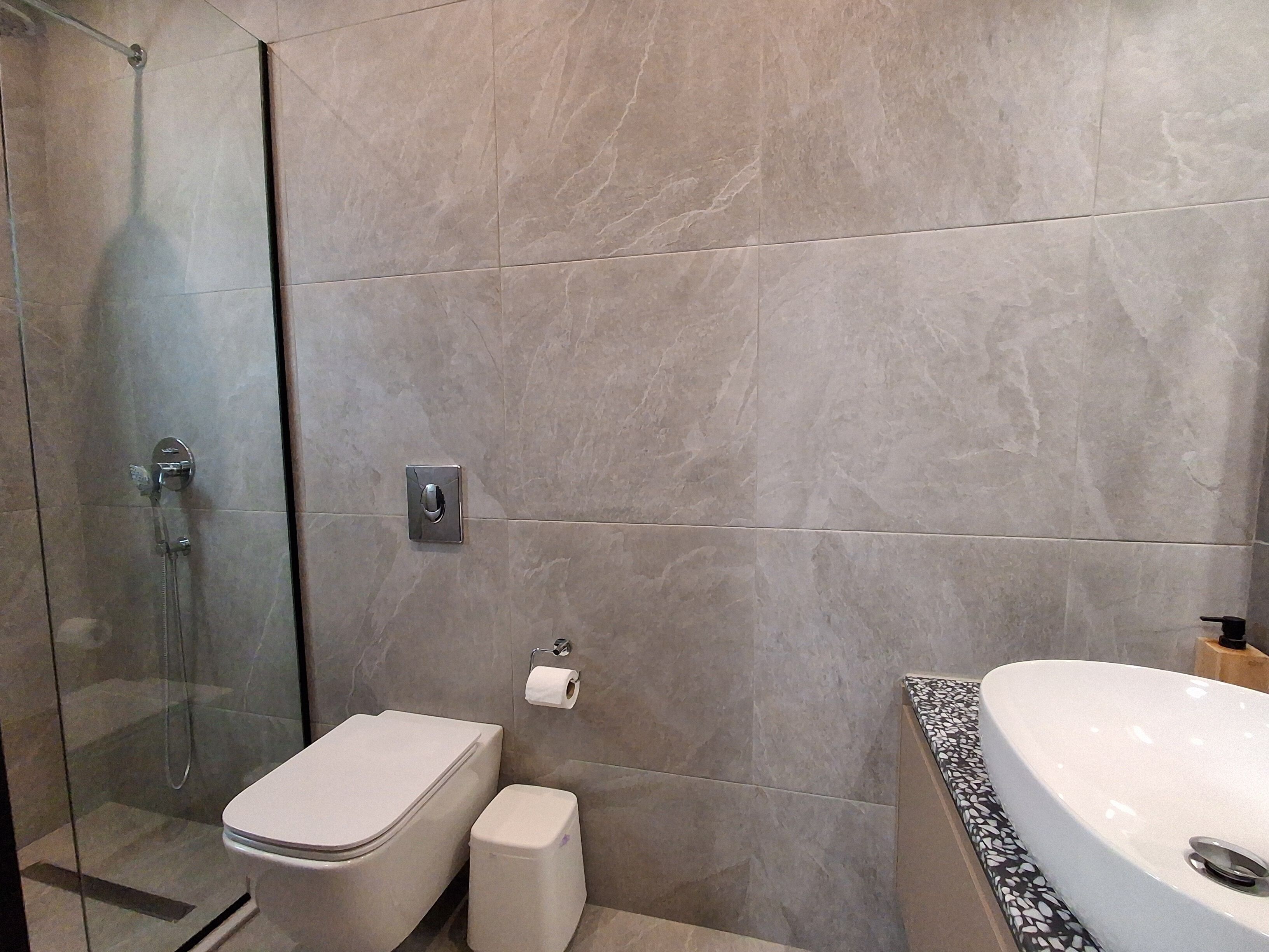 A modern bathroom with a glass-enclosed shower, a toilet, a sink with a marble countertop, and a toilet paper holder on the wall.