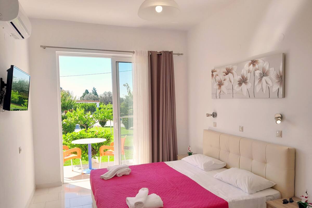 Ein Hotelzimmer mit Bett, Fernseher, einem Gemälde und Blick auf einen Garten.