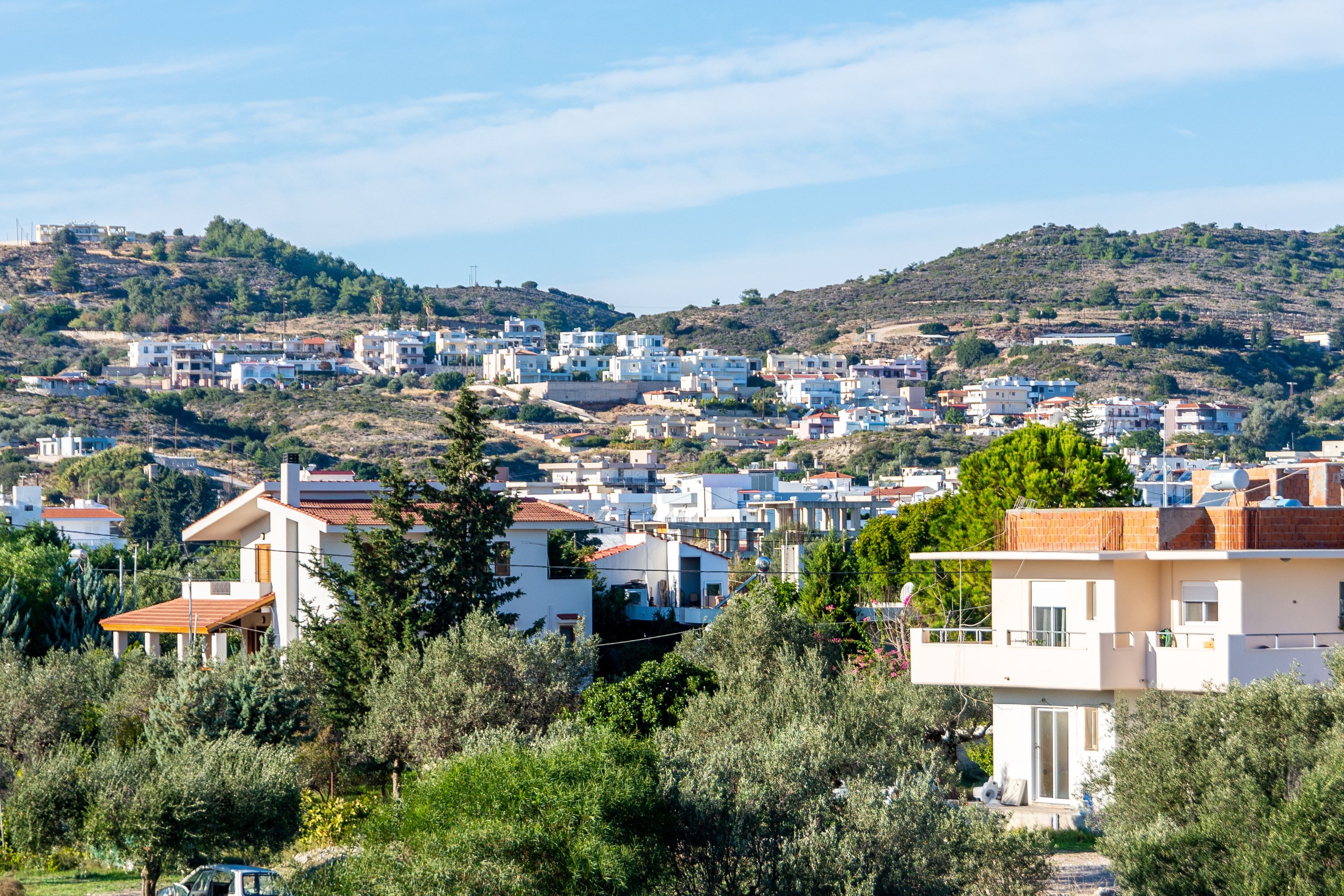 A residential area with modern houses, dense vegetation, and a hilly backdrop.