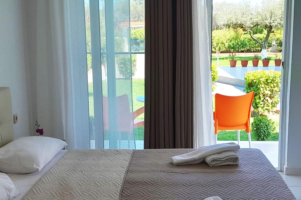 Ein Schlafzimmer mit einem großen Bett, einem Fenster mit Vorhängen und Blick auf einen Garten.
