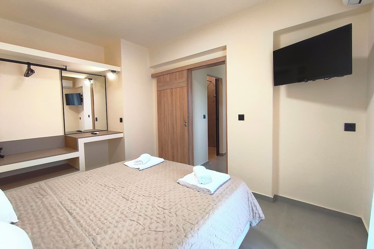 Ein Schlafzimmer mit einem Bett, einem Nachttisch, einem Spiegel, einem an der Wand montierten Fernseher und einem Kleiderschrank.