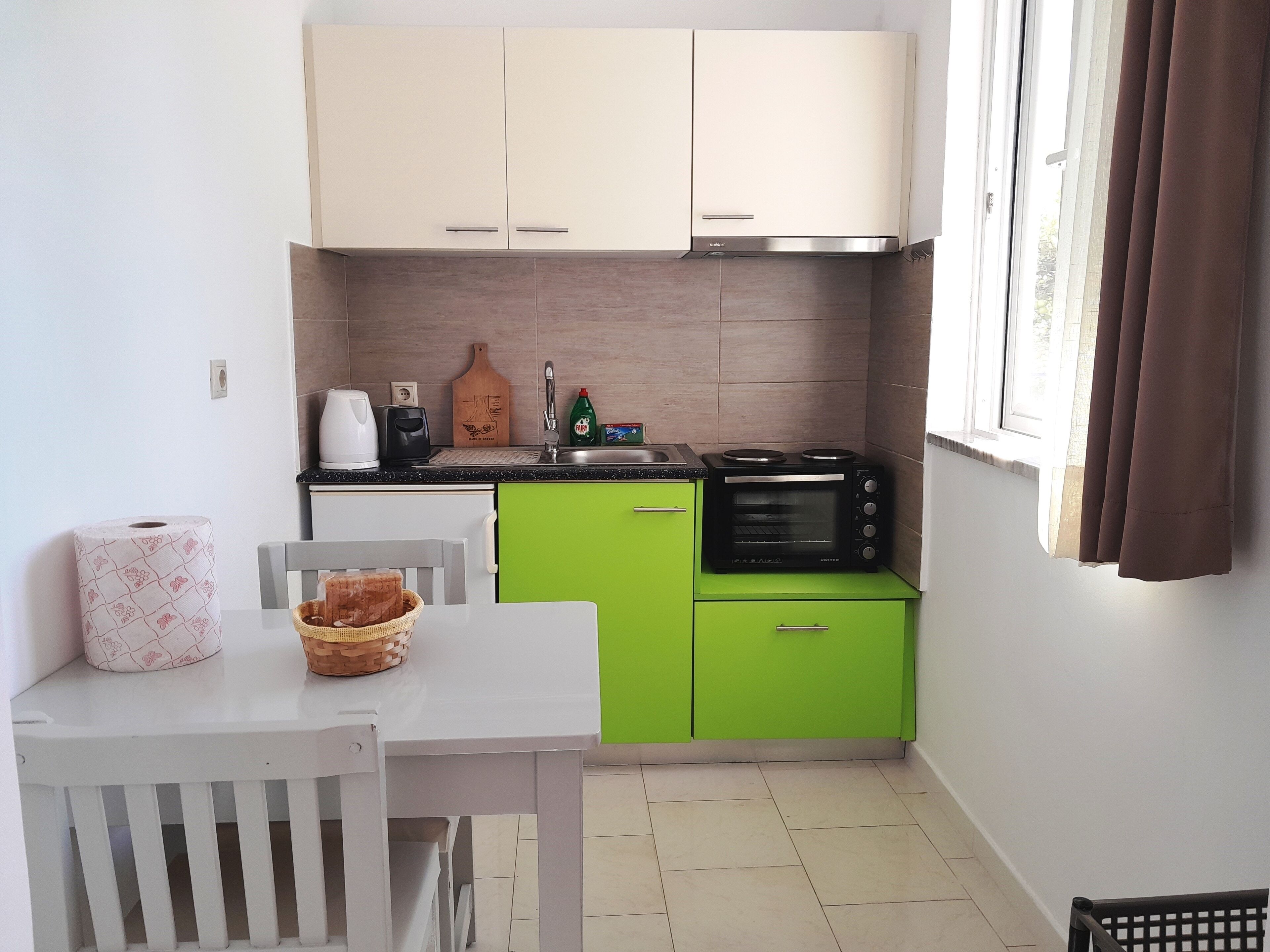 A compact kitchen with a white table, green cabinets, a black microwave, and a window with curtains.