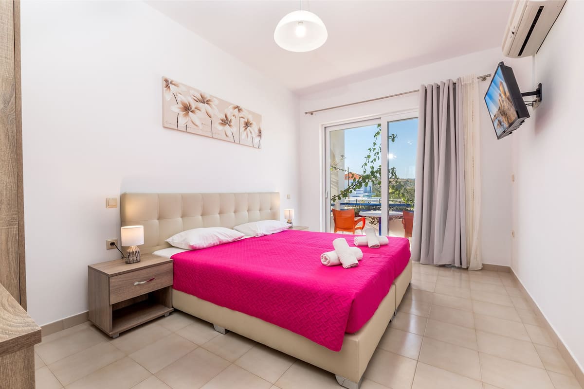 Ein Hotelzimmer mit Bett, Nachttisch, Lampe, Fernseher und Blick ins Freie.