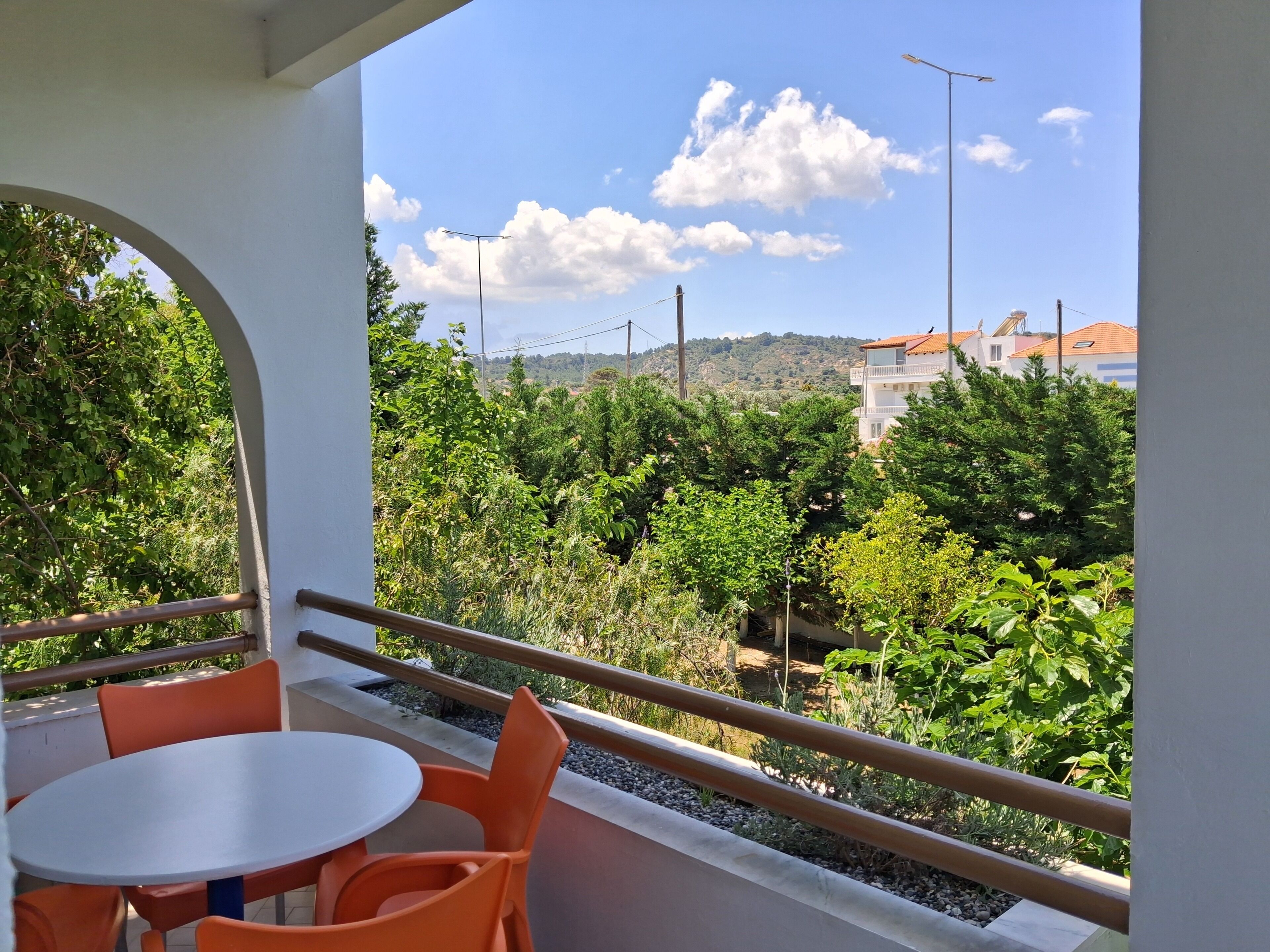 Un balcon avec une table et des chaises, donnant sur un jardin et des immeubles.