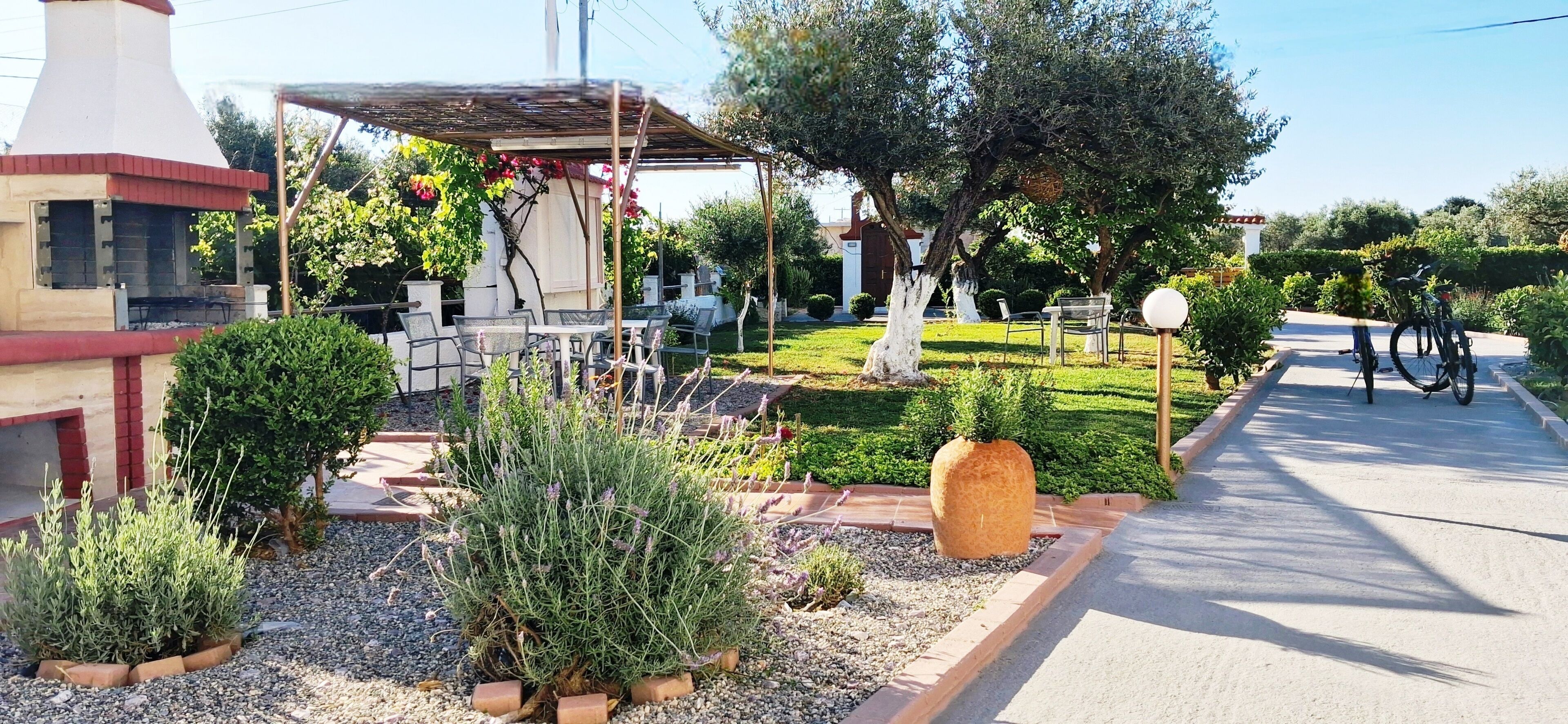 Eine Terrasse mit Sitzgelegenheiten im Freien, einer Pergola und einem Garten mit verschiedenen Pflanzen und einem großen Felsen als Blickfang.
