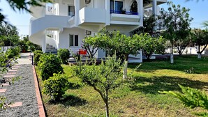 Un bâtiment moderne à deux étages, doté d’un toit plat, d’un balcon à l’étage supérieur et d’un petit jardin agrémenté d’un chemin menant à l’entrée.