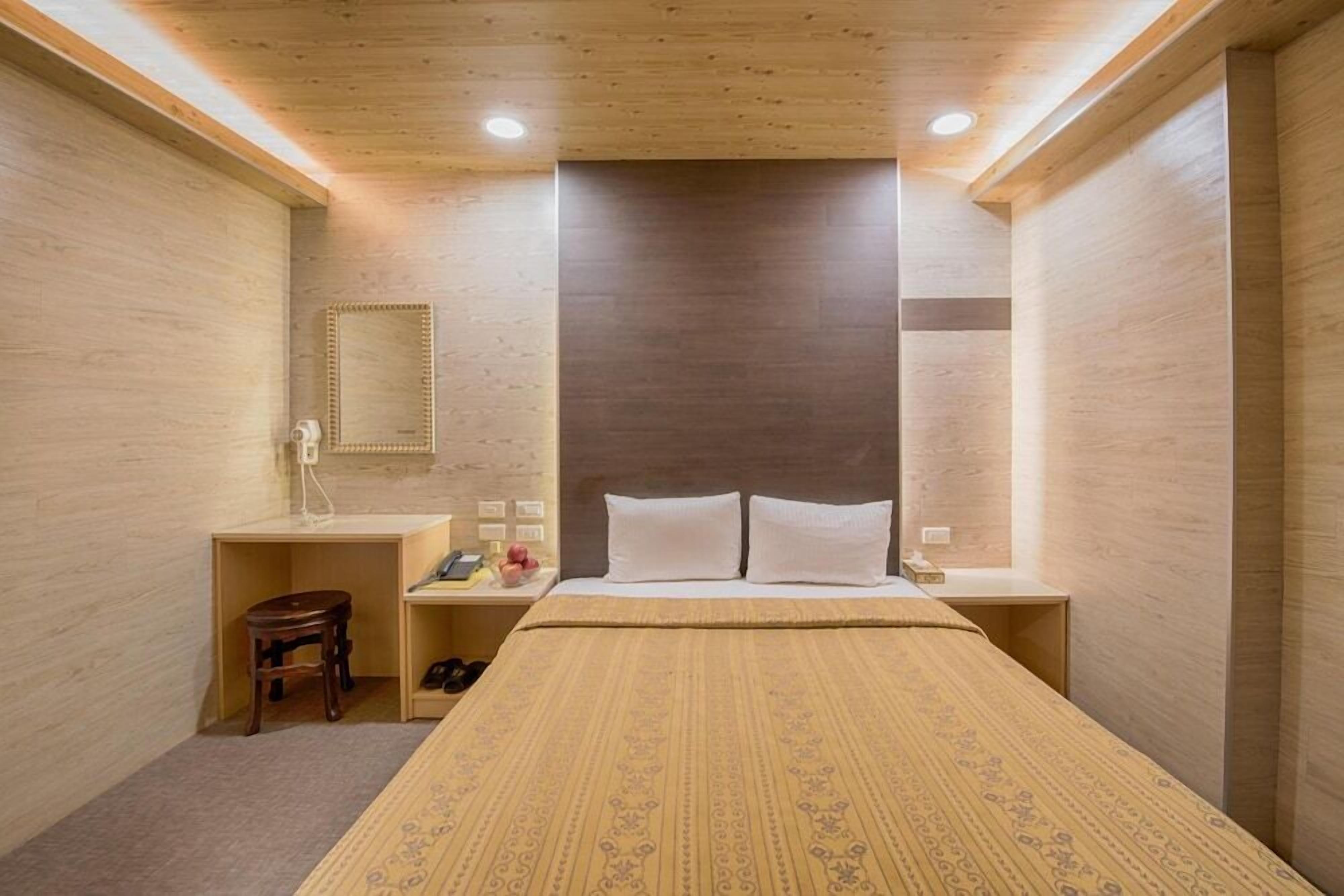 A hotel room with a bed, a desk, a chair, a mirror, and a nightstand.