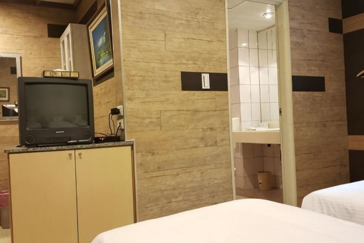 A hotel room with a bed, a television on a cabinet, a bathroom with a mirror, and a tiled wall.