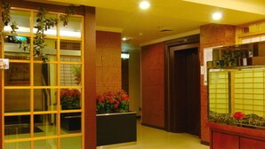 A hotel lobby with a reception desk, a glass partition with plants, and a tiled floor. - Empire Hotel (Taipei)