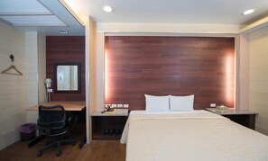 A hotel room with a bed, a desk, a chair, a mirror, and a nightstand. - Empire Hotel (Taipei)