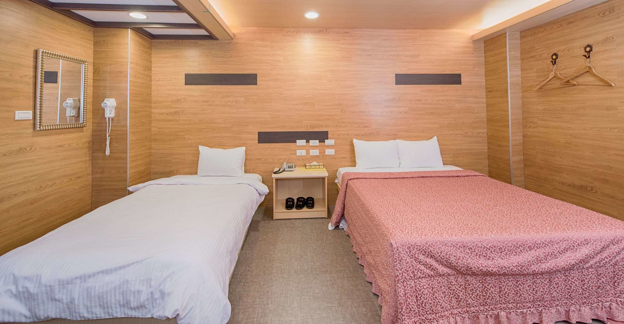 Habitación de hotel con dos camas, una mesita de noche con teléfono y espacio para zapatos, un espejo y paredes de madera.