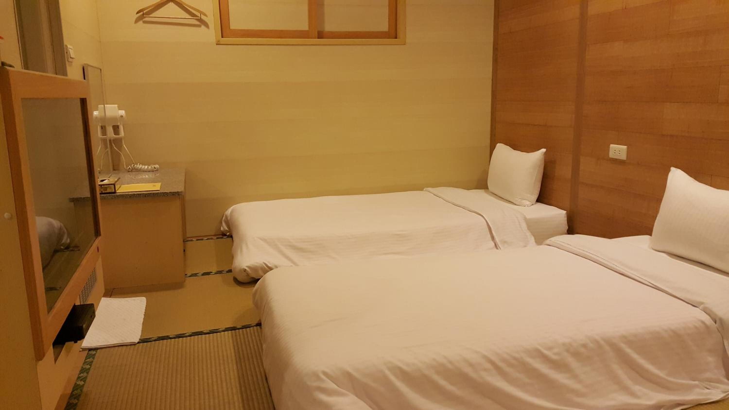 A hotel room with two beds, a wooden headboard, a small bedside table with a lamp, and a mirror.