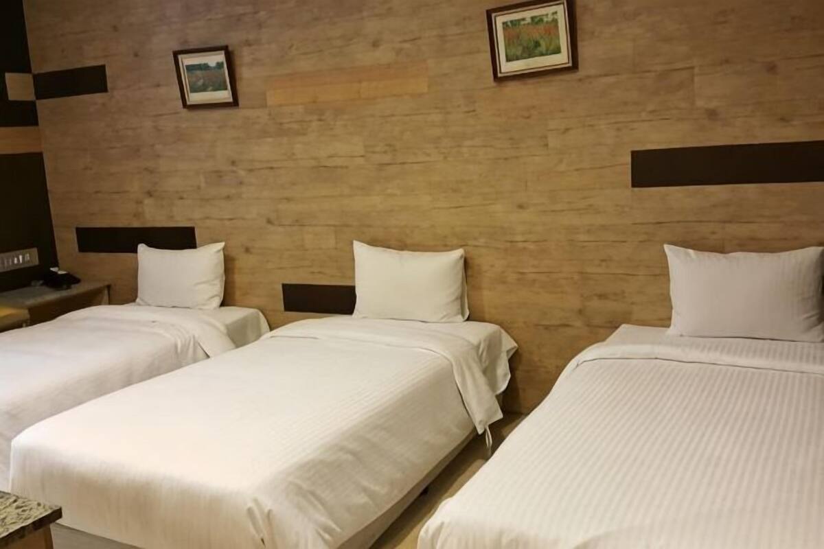 A hotel room with three single beds, wooden headboards, and a wooden wall.