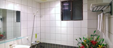 A bathroom with a white sink, a bathtub with dark tiles, a shower, and a window with a towel rack.