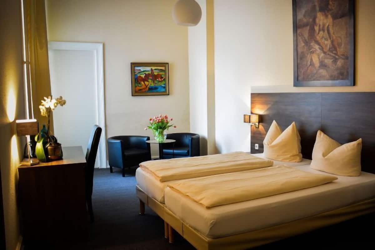 Habitació d'hotel amb llit doble, escriptori amb làmpada, cadira, taula petita amb flors i dues làmpades penjades a la paret.