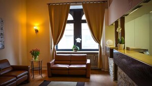 Een gezellige woonkamer met een bruine leren bank, een klein bijzettafeltje met een bloevas, en een raam met gordijnen.