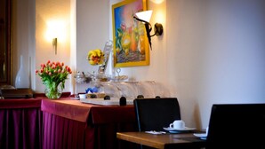 Een eethoek met een tafel gedekt voor twee personen, een bloevas, een schilderij aan de muur en een buffet met diverse gerechten.