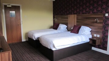 Una cama doble con sábanas blancas, cabecera de madera y pared con un diseño oscuro.