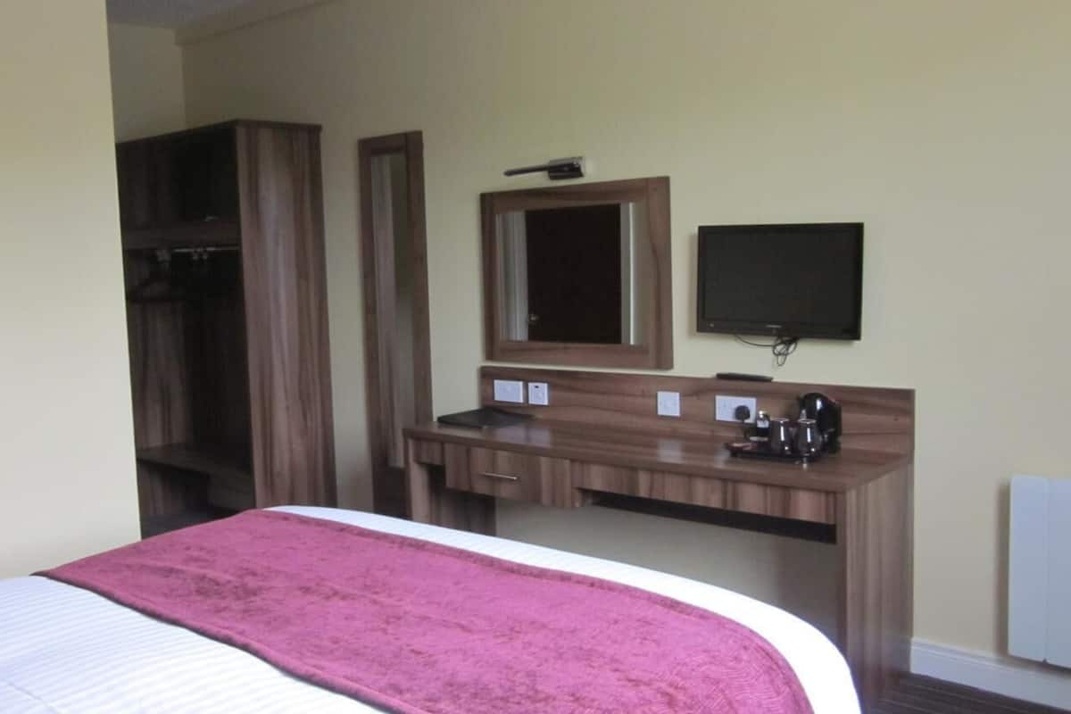 A hotel room with a bed, a wooden desk with a mirror, a television, and a coffee maker.