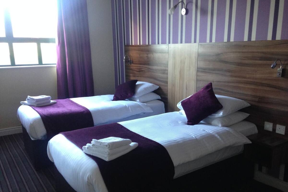A hotel room with two beds, each with a purple blanket and pillows, and towels on the beds.