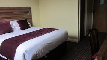 Una habitación de hotel con una cama grande, un cabecero de madera, una alfombra oscura y un escritorio de madera con una silla.