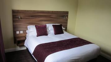 Una cama bien hecha con cabecera de madera, ropa blanca y dos almohadas oscuras.
