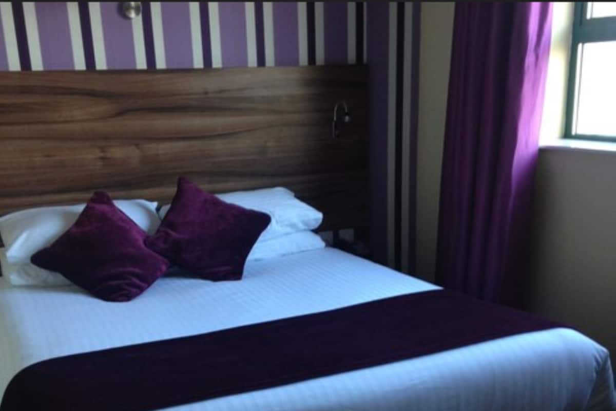 A bed with a wooden headboard, white bedding, and two purple pillows.