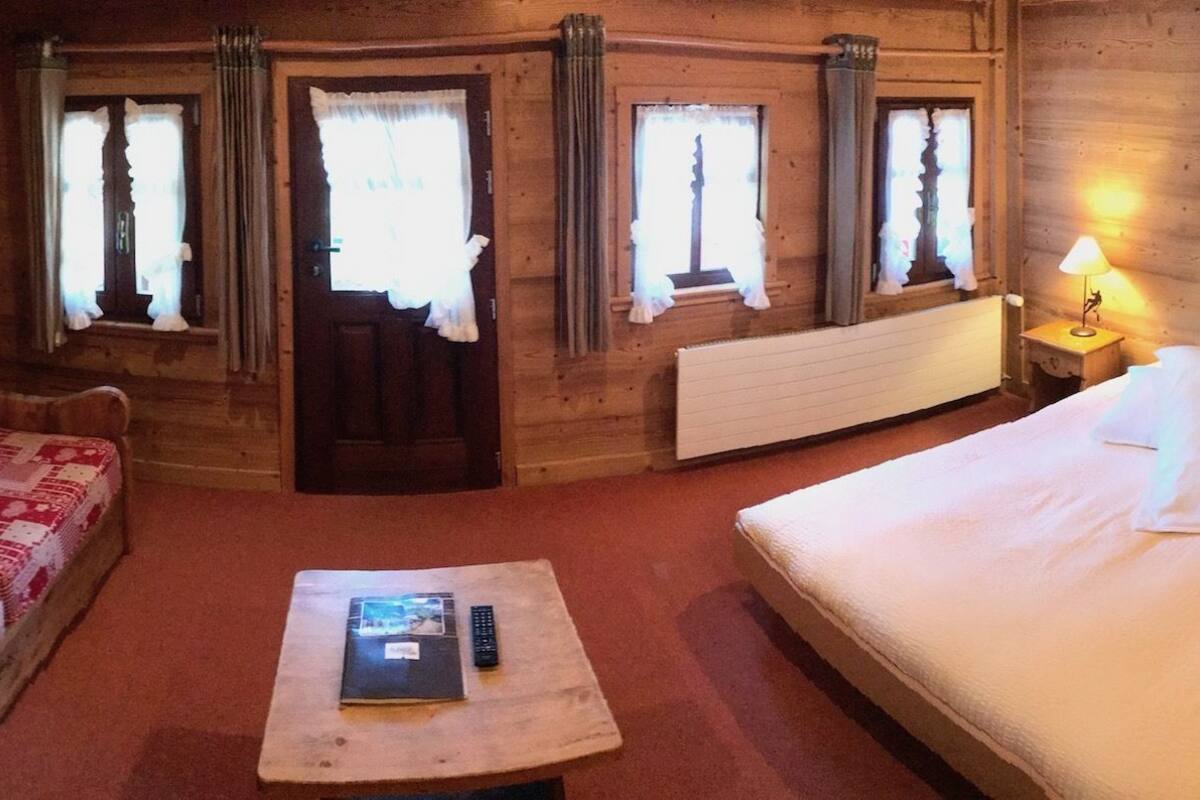 Una habitación acogedora de madera con un sofá, una cama, una mesa con un libro y un control remoto, y dos lámparas de noche.