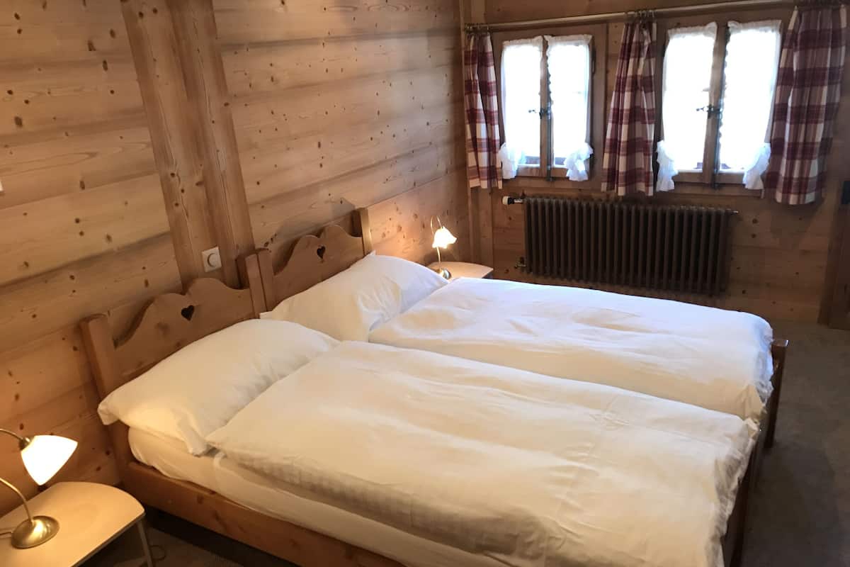 Una habitación tipo cabaña de madera con dos camas individuales, una mesita de noche con lámpara y una ventana con cortinas escocesas.