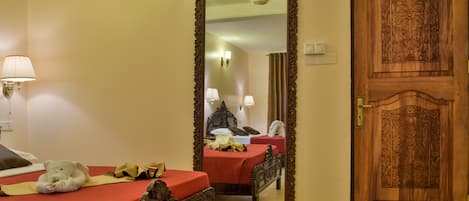 Habitación de hotel con cama de madera, un espejo grande, una puerta de madera y una colcha roja.