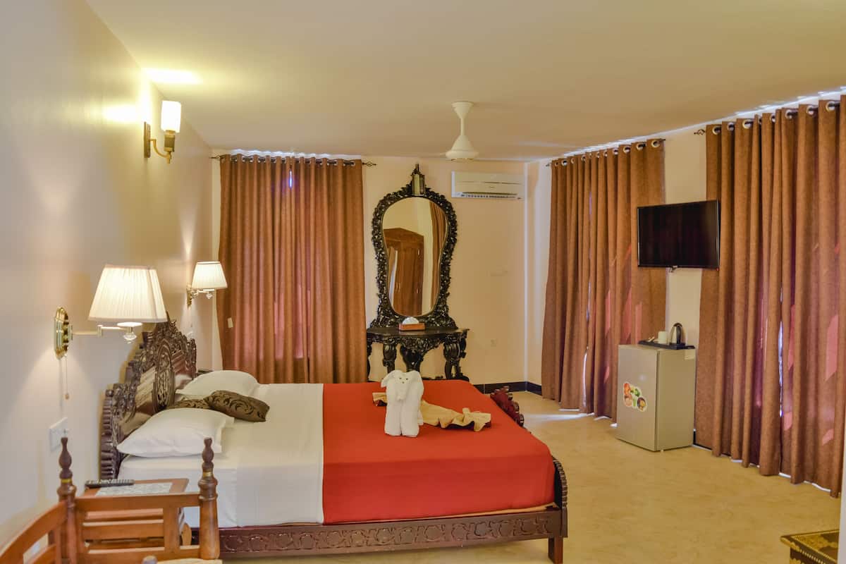 A hotel room with a large bed, a dresser, a television, and a mirror.