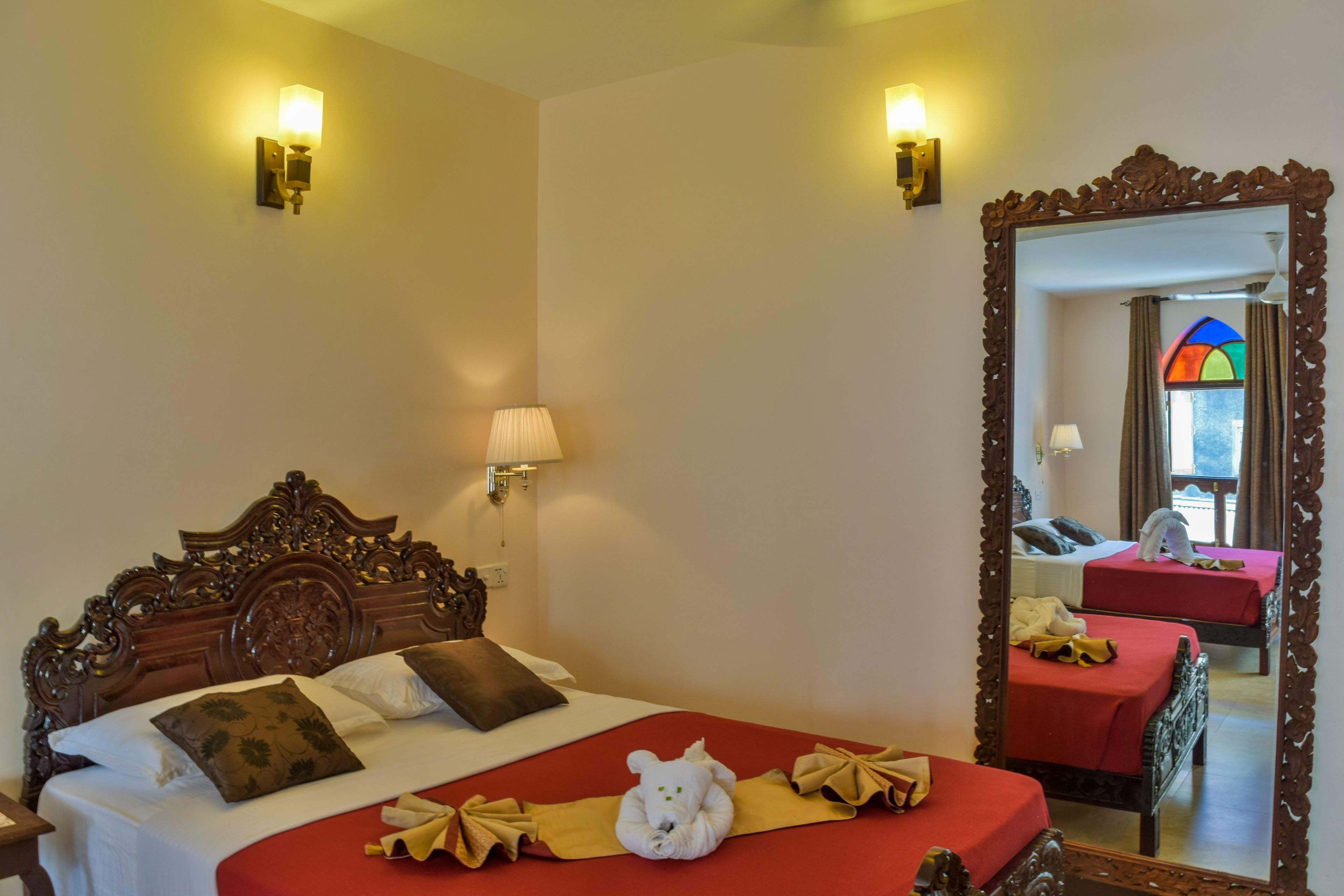 A hotel room with a large bed, a wooden headboard, two bedside lamps, and a mirror with an ornate frame.
