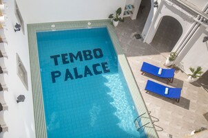 A rooftop pool with "TEMBO PALACE" written on the water, two lounge chairs, and a potted plant.