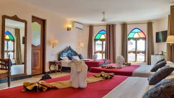 Una camera d'albergo con due letti, un grande specchio, una testiera in legno, una televisione e una finestra con vetrate artistiche.