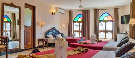A hotel room with two beds, a large mirror, a wooden headboard, a television, and a window with stained glass.
