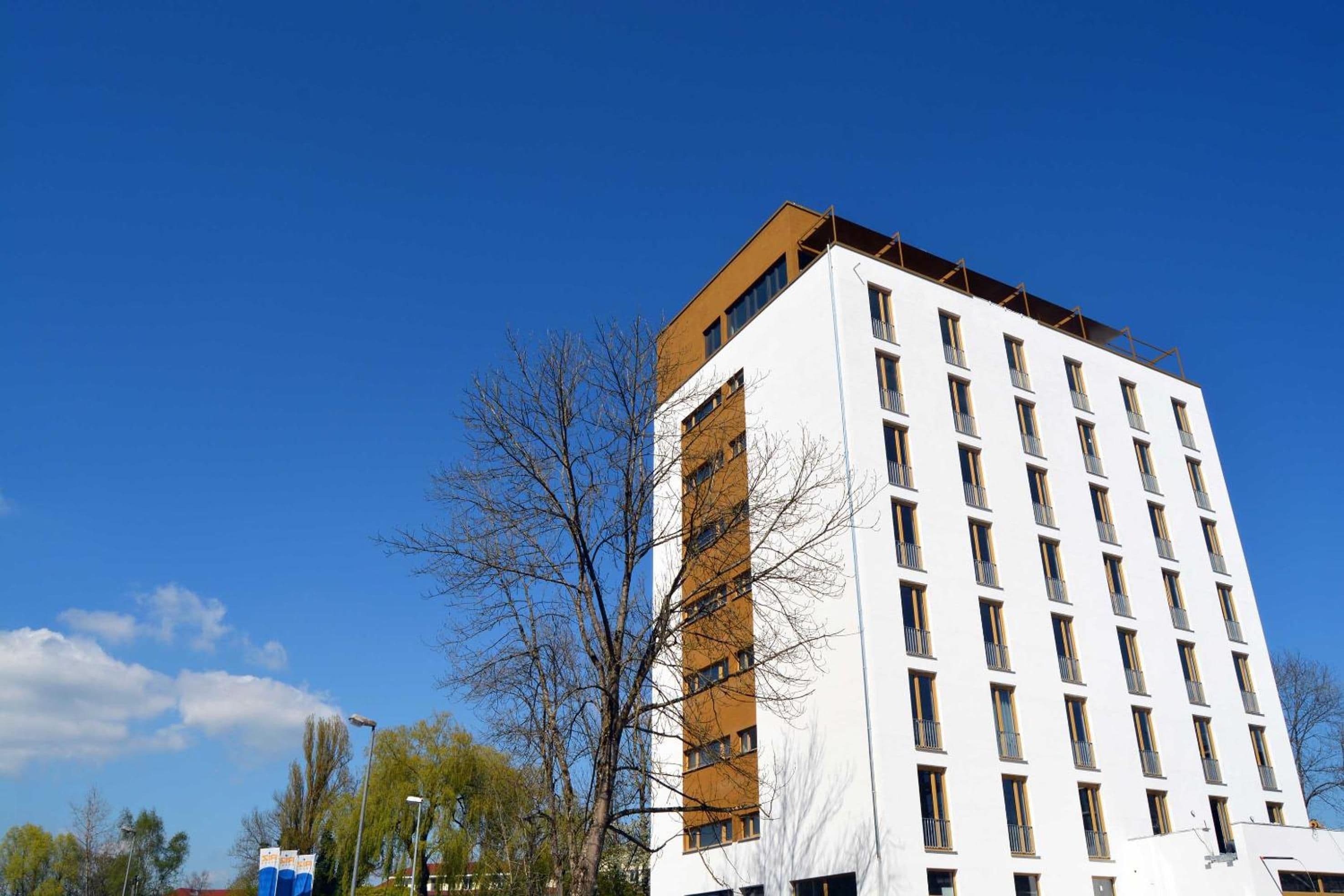 Un immeuble à plusieurs étages, doté d’une façade blanche et d’une partie supérieure de couleur brun clair.