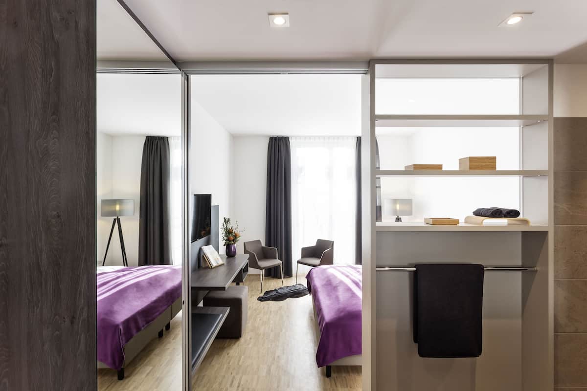 Een moderne hotelkamer met een bed, bureau, stoelen en een spiegel.