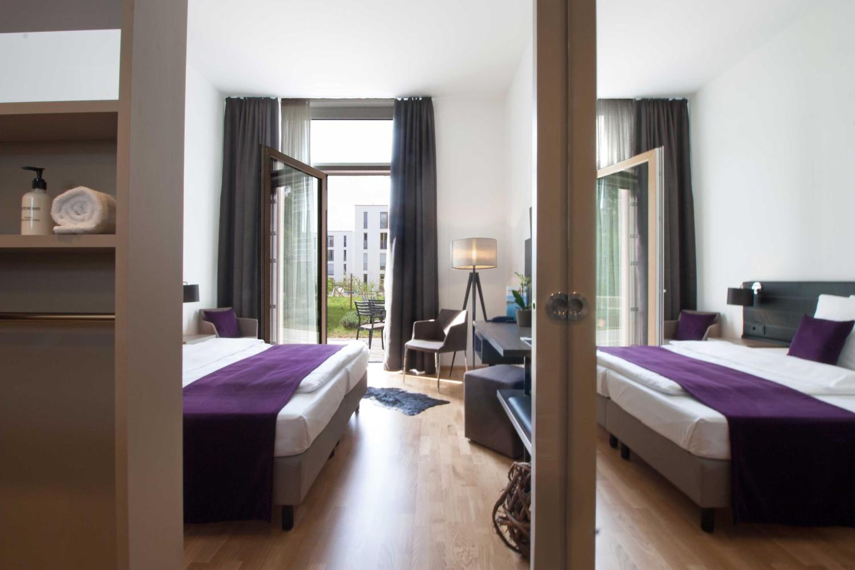 Une chambre d’hôtel avec deux lits, un bureau, une chaise, une lampe et une vue sur l’extérieur.