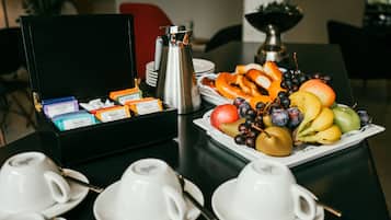 Une table mise pour le petit-déjeuner, avec une machine à café, une assiette de fruits et une boîte de sachets de thé.