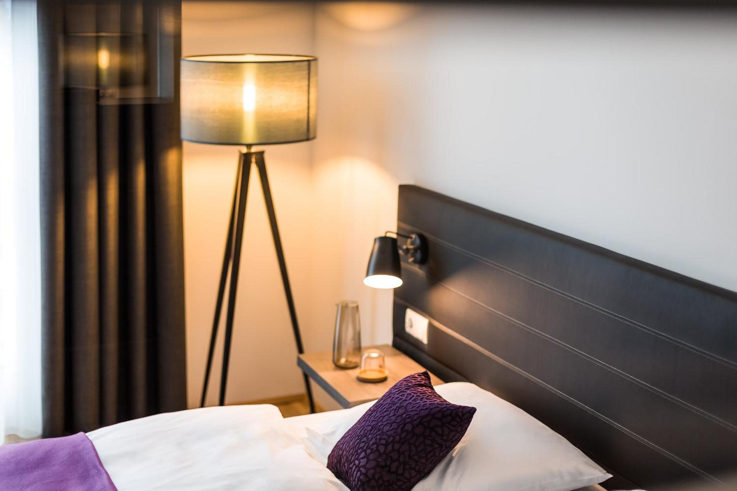 Ein Hotelzimmer mit einem Bett, einer Nachttischlampe und einem Nachttisch mit einem Glaskrug.