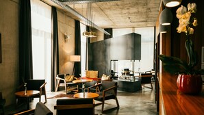 A modern hotel lobby with a mix of seating areas, a reception desk, and a large window providing natural light. - Hotel K99 (Radolfzell am Bodensee)