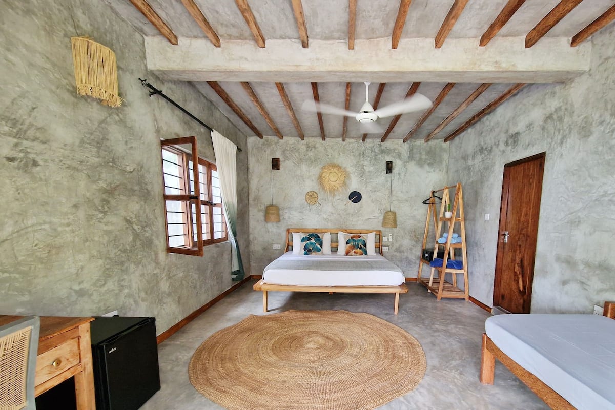A bedroom with a bed, a desk, a wardrobe, a ceiling fan, and a woven rug.