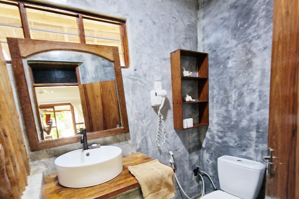 Un baño con tocador de madera, un lavamanos blanco, un espejo, una toalla, un inodoro y una pared de mármol.