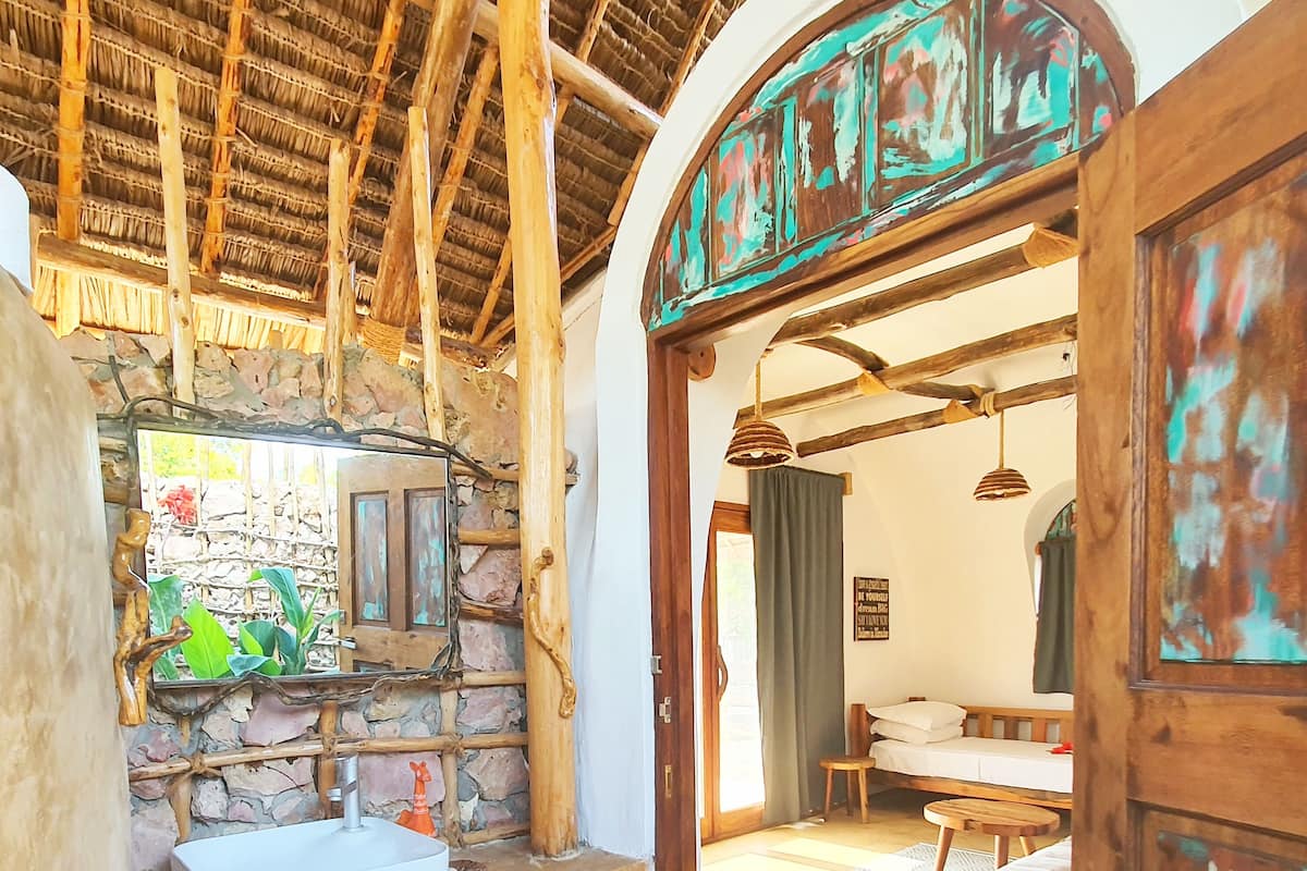 A rustic bathroom with a stone wall, wooden beams, and a large mirror.
