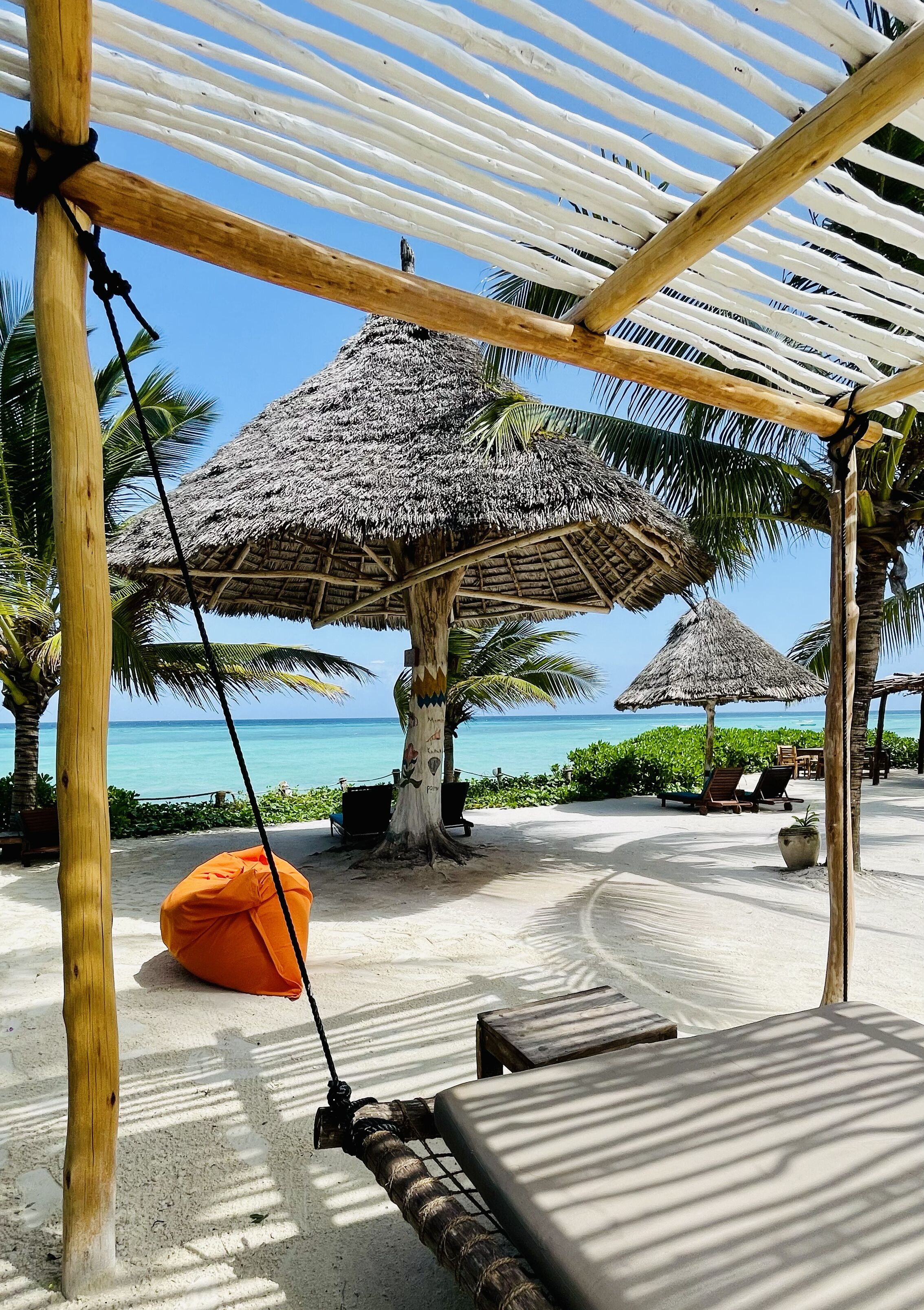 A beachside lounge with thatched umbrellas, lounge chairs, and a swing.