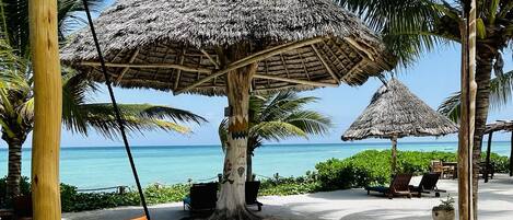 A beachside lounge with thatched umbrellas, lounge chairs, and a swing.