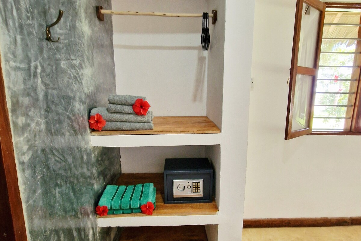 Una habitación con pared de mármol, estante de madera con toallas dobladas y una radio, y ventana con marco de madera.